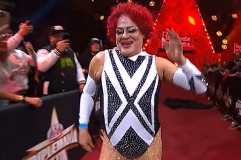 El luchador exótico Pimpinela Escarlata saluda al público durante su entrada al ring. La nota detalla la anécdota del luchador con Triple H y la reacción del directivo.