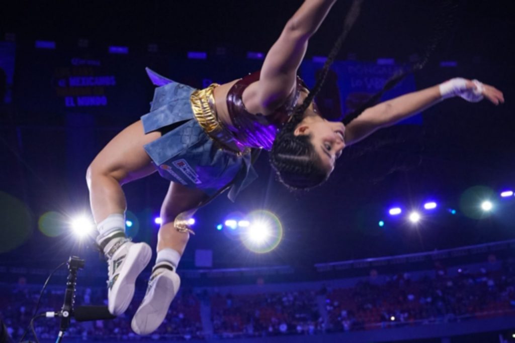 Alana Flores realiza una acrobacia en el ring durante el evento Supernova Strikers. La nota informa sobre las ganancias de la streamer, estimadas en un millón de pesos por su combate de boxeo.