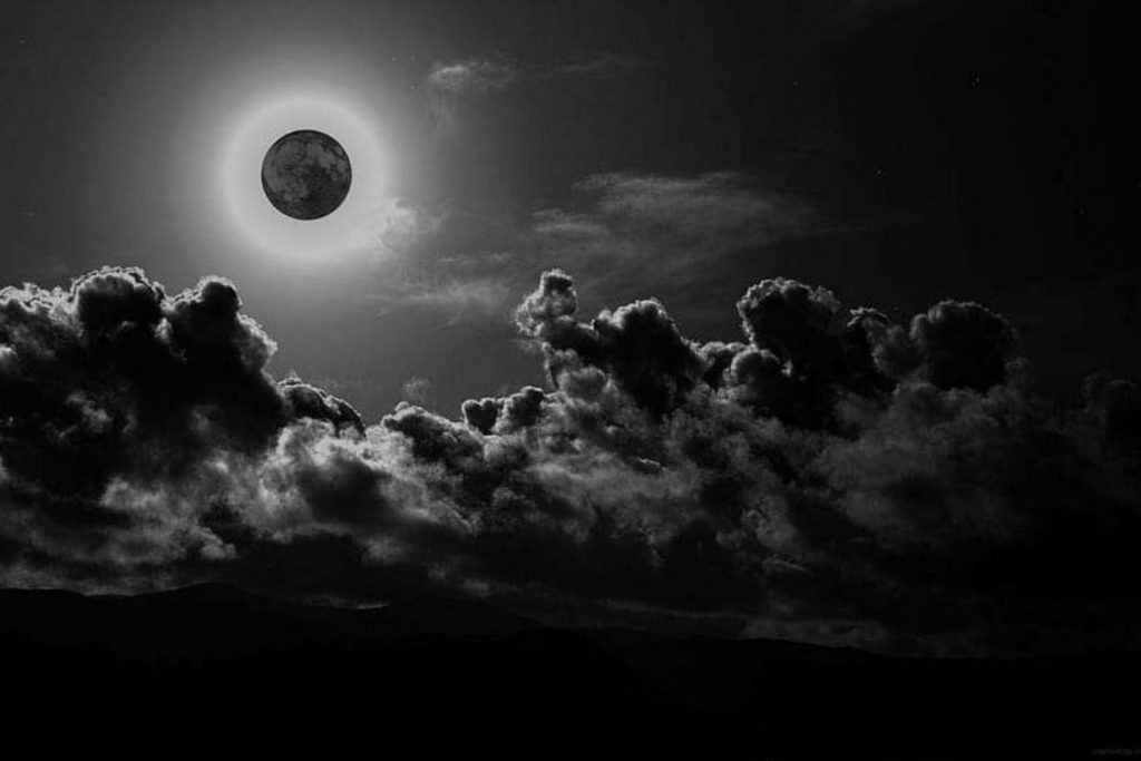 Representación artística de la Luna Negra sobre un cielo nocturno con nubes. Este fenómeno astronómico, que es una luna nueva, se ilustra con un disco oscuro y un halo de luz, simbolizando su invisibilidad.