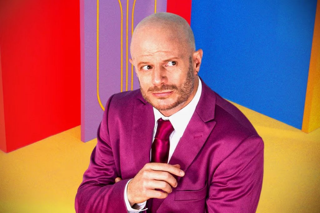 El conductor y comediante Facundo con un traje morado. La nota explora la participación del famoso en el reality show