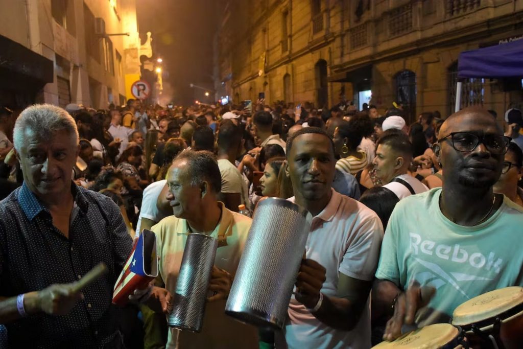 Músicos tocando percusiones como el güiro y las congas en una fiesta callejera. La nota destaca que la música en vivo es el corazón de los festivales de salsa.
