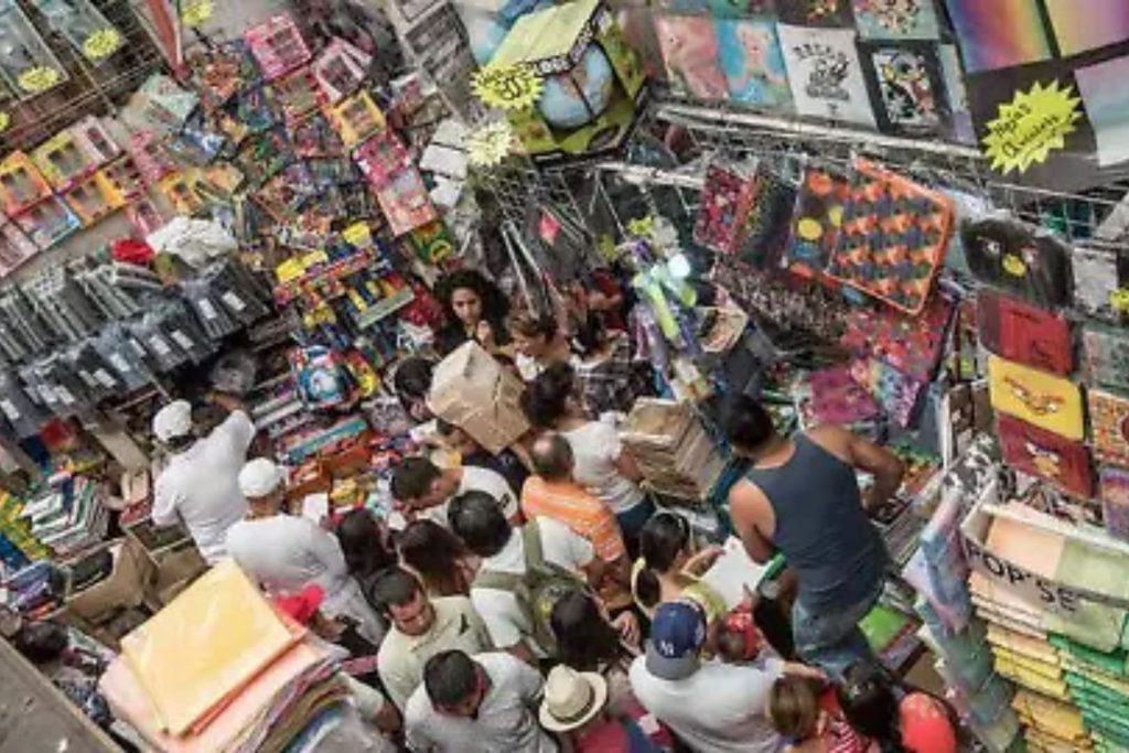 Vista aérea de una papelería abarrotada de gente comprando útiles para el regreso a clases. La nota da consejos para realizar las compras de forma segura y económica.