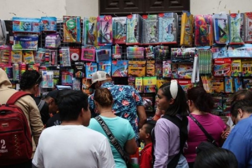 Padres de familia y niños frente a un muro de útiles escolares. La nota detalla cuáles son los artículos de la lista oficial de la SEP y sus precios promedio.