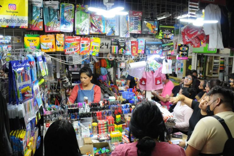 Un puesto de papelería atendiendo a muchos clientes por la noche. La nota da consejos para las compras de última hora para el regreso a clases.