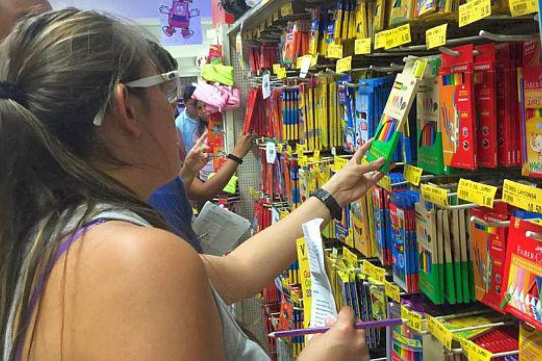 Una mujer eligiendo una caja de colores en una papelería. La nota compara precios de útiles escolares en supermercados y tiendas del centro para encontrar la mejor opción.