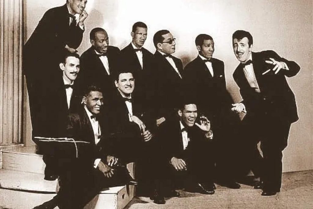 Los músicos de la Sonora Matancera en una divertida foto grupal. La nota celebra la alegría y el sabor que la orquesta transmitía en su música y presentaciones.
