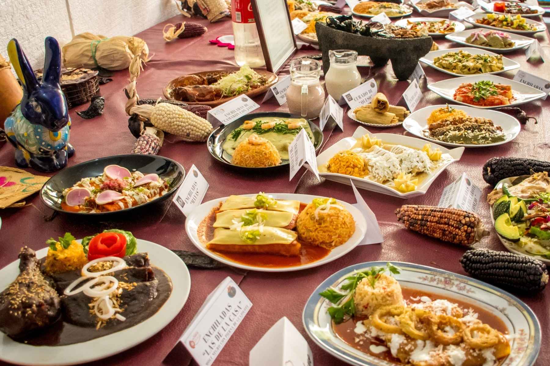 Una mesa con la gran variedad de platillos de la Feria de la Enchilada. La nota informa que hay más de 200 tipos de enchiladas para probar en el evento.