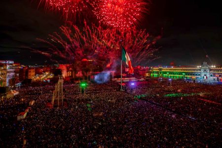 El Zócalo de la CDMX lleno de gente durante la celebración del Grito de Independencia. La nota informa sobre el concierto gratuito del 15 de septiembre.