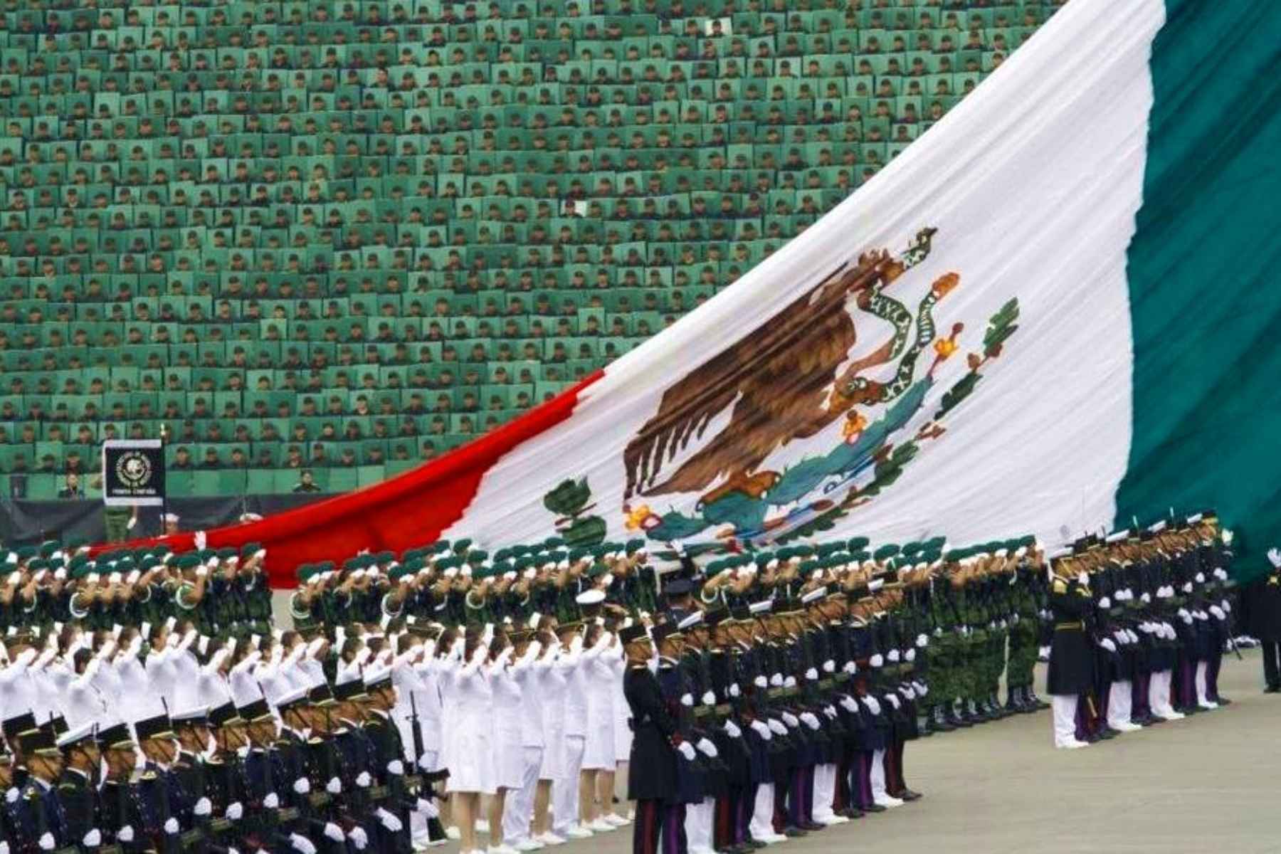Una bandera monumental de México desplegada en el Zócalo frente a un mosaico humano. La nota destaca la organización y disciplina del Desfile Militar.