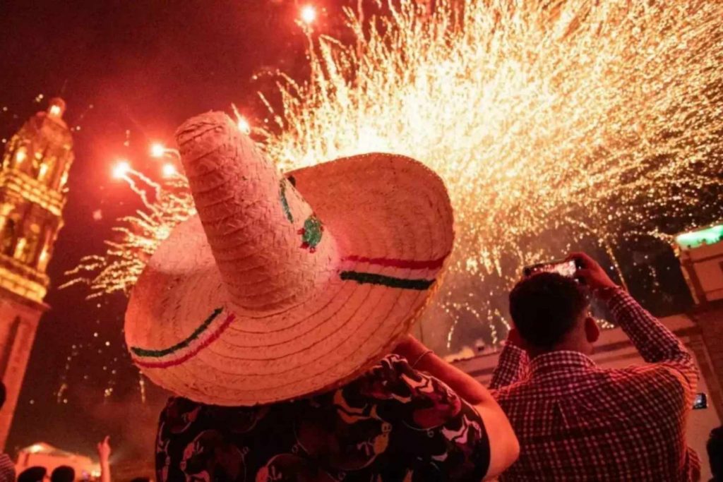 Una persona con sombrero de charro observa el espectáculo de fuegos artificiales durante la Noche Mexicana. La nota celebra las tradiciones que hacen única esta fiesta.