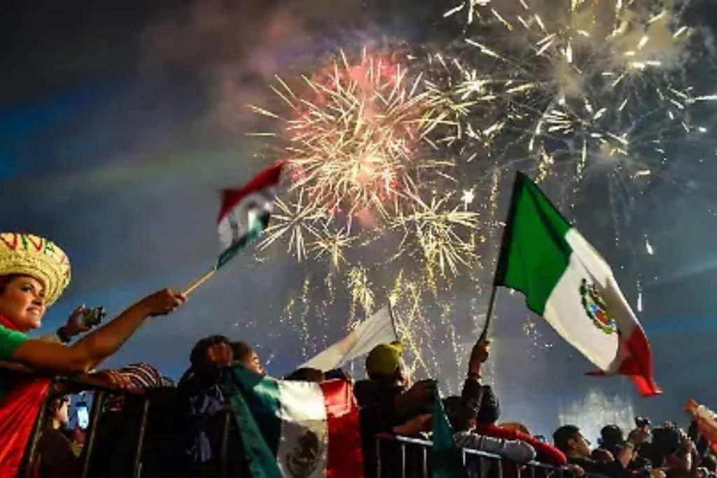 Mexicanos celebrando la Noche del Grito con banderas y fuegos artificiales. El artículo habla sobre el orgullo y la emoción que nos une como pueblo cada 15 de septiembre.