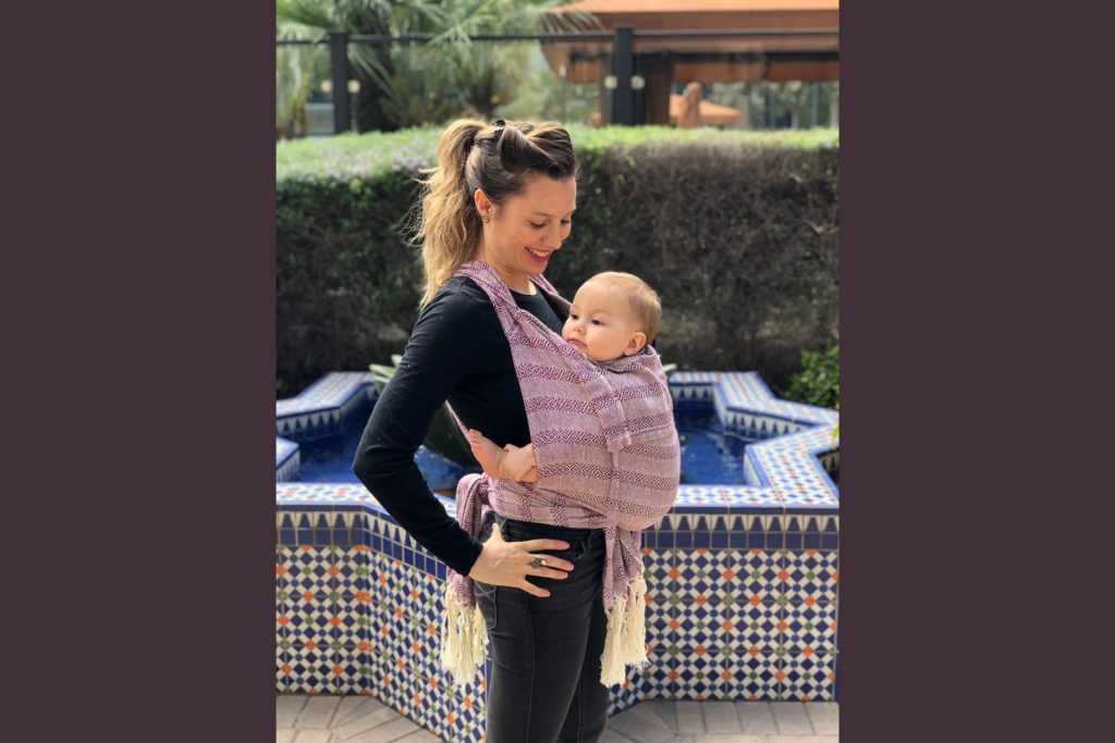 Una mamá cargando a su bebé de forma segura y cómoda con un rebozo. La nota destaca el uso tradicional del rebozo como portabebés.