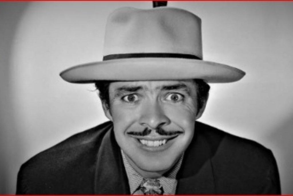 Un primer plano en blanco y negro del comediante Germán Valdés "Tin Tan" con una sonrisa pícara. La nota explora el legado del Pachuco de Oro.