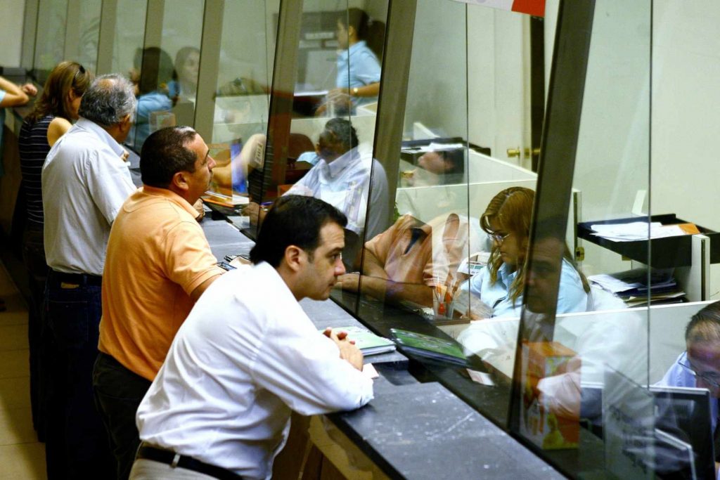Clientes realizando trámites en la ventanilla de una sucursal bancaria. La nota informa si los bancos abrirán el 15 y 16 de septiembre por las Fiestas Patrias.