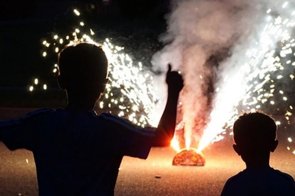 Dos niños a contraluz viendo fuegos artificiales en la calle. La nota habla sobre las tradiciones de la Noche Mexicana, incluyendo la pirotecnia.