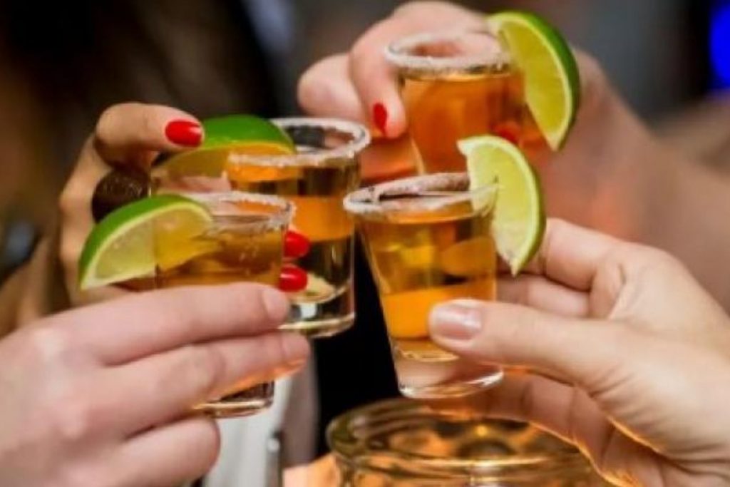 Un grupo de amigos brindando con caballitos de tequila. La nota celebra las bebidas tradicionales que acompañan la Noche Mexicana.