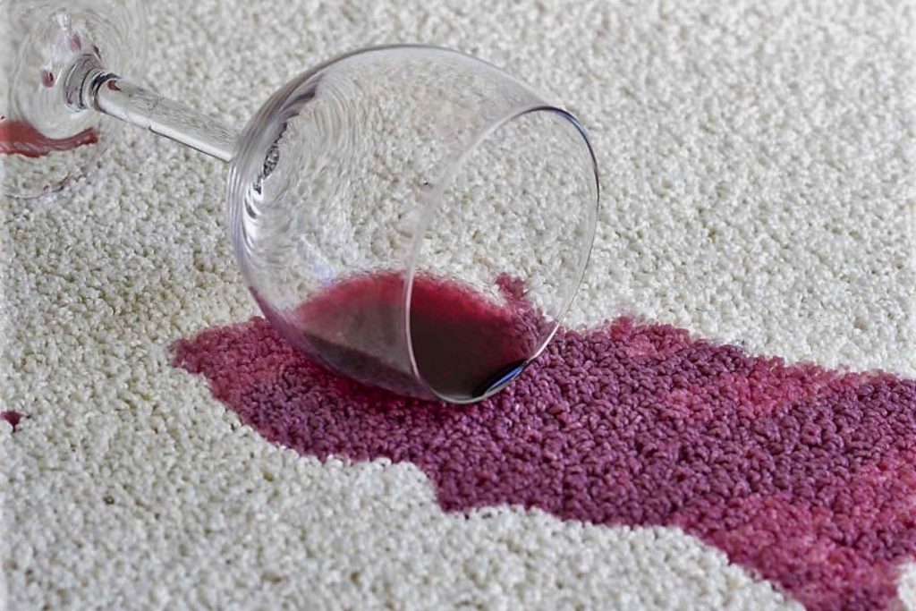  Una copa de vino tinto derramada sobre una alfombra blanca. La nota habla con humor sobre los pequeños accidentes que ocurren en las fiestas.
