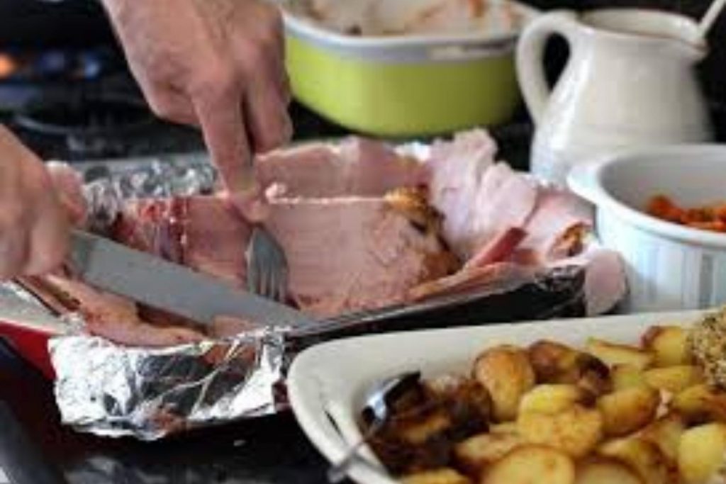 Una persona cortando rebanadas de jamón horneado para la cena. La nota habla sobre los platillos que son el centro de las celebraciones familiares.