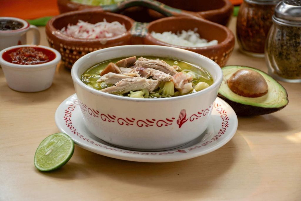 Un plato de pozole verde estilo Guerrero, servido con aguacate y chicharrón. La nota comparte la receta para preparar este platillo único y lleno de sabor.