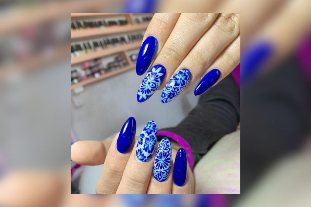 Uñas largas de color azul con diseños blancos inspirados en la Talavera poblana. La nota ofrece ideas creativas que van más allá del tricolor.